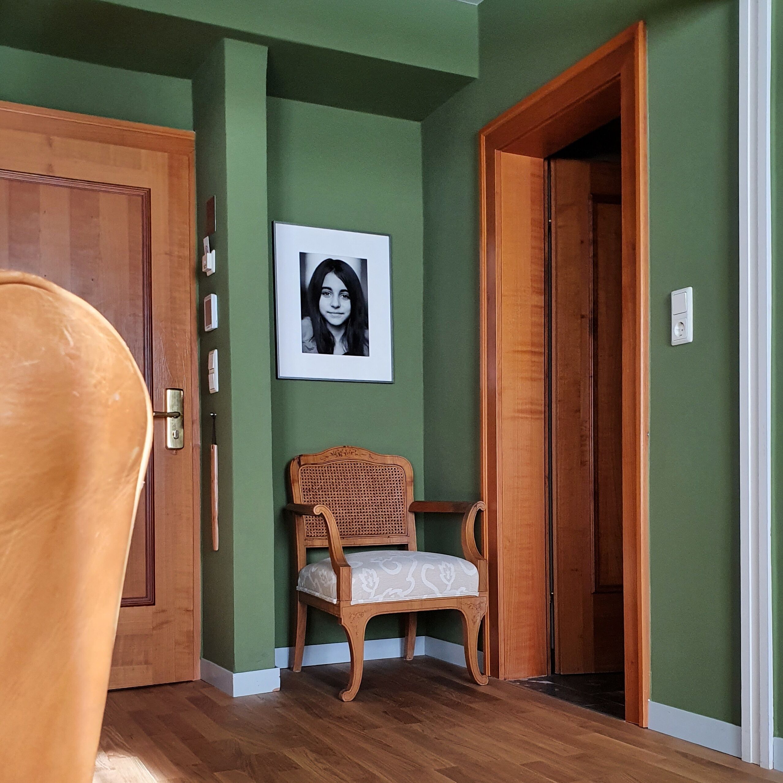 Ein Zimmer mit einem Holzsessel, einem gerahmten Bild an der Wand und einer Tür zu einem anderen Raum.