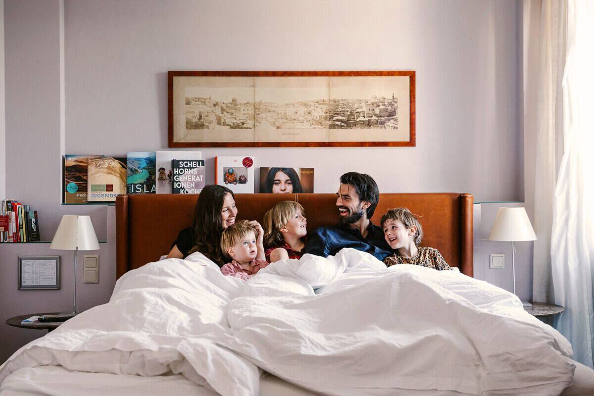Una familia de seis personas en una habitación de hotel con una cama grande, una mesita de noche con una lámpara y un cuadro en la pared.