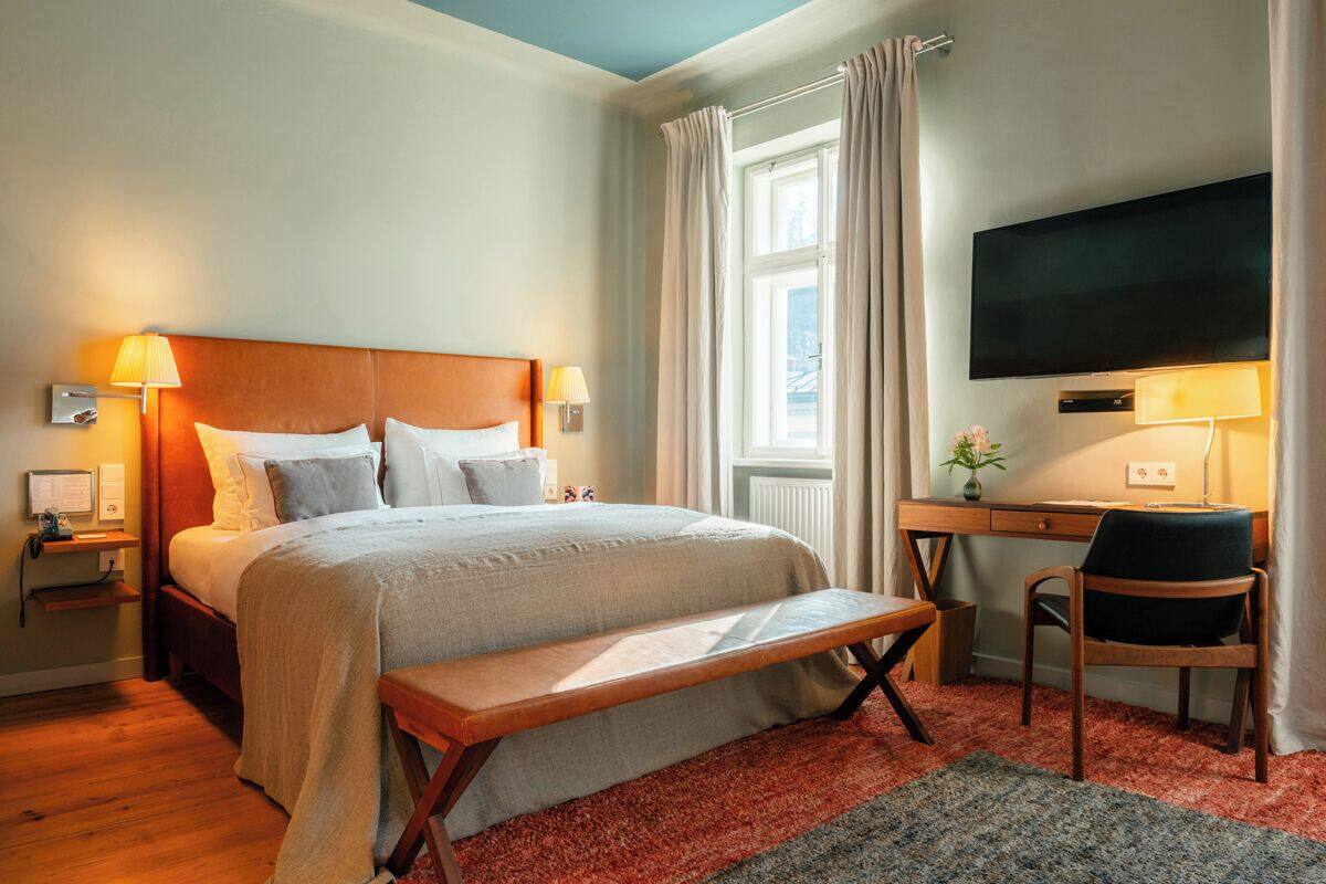 Habitación de hotel con cama, mesitas de noche, escritorio con silla, televisor y ventana con cortinas.