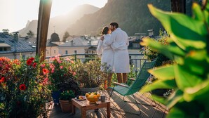 A couple embracing on a balcony with potted plants, a table with fruit, and a view of buildings and mountains in the background. - Boutique Hotel Auersperg (Salzburg)