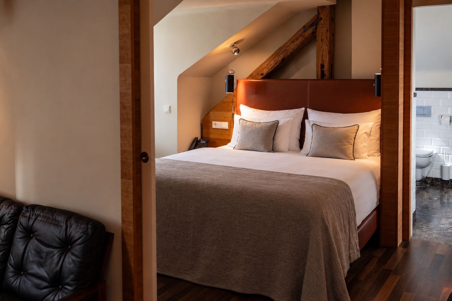 Une chambre avec un grand lit, une tête de lit en bois et une vue sur la salle de bain.