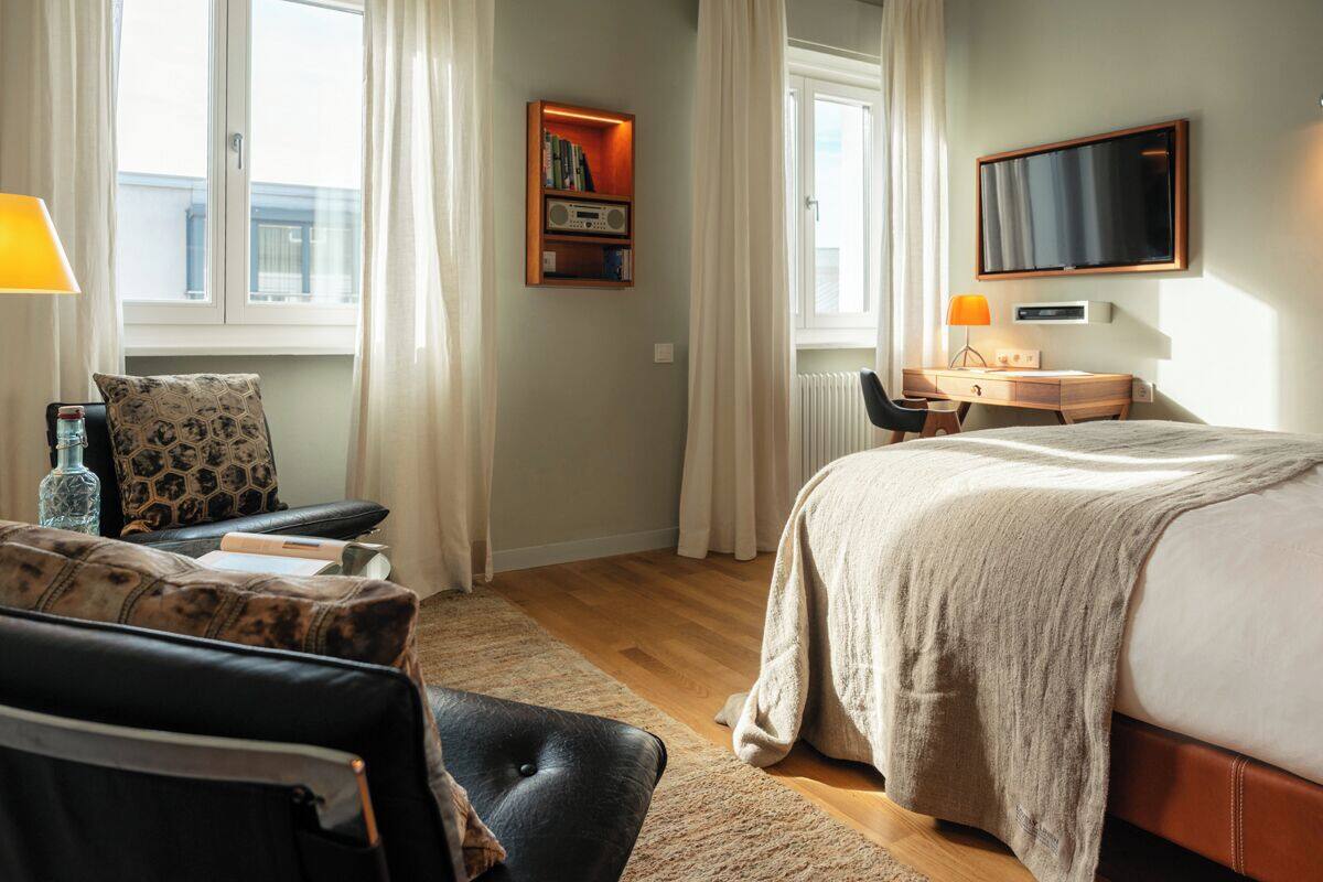 Habitación de hotel con cama, escritorio con silla, estantería y televisor en la pared.