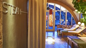 A spa area with a sign reading "STEAM," wooden flooring, lounge chairs, and a large window with a view of the outside.