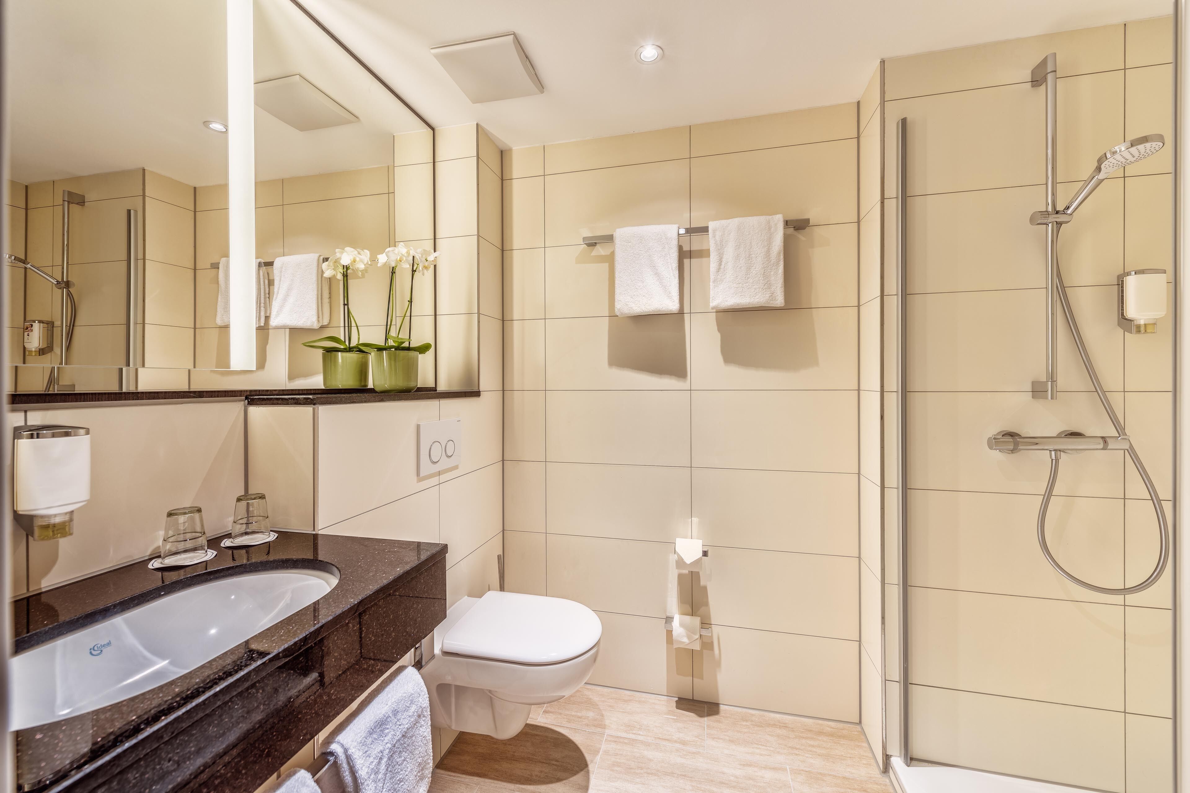 A modern bathroom with a large mirror, a sink, a toilet, and a shower area.