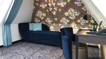 A cozy room with a blue sofa, a desk with a lamp, and a colorful stained glass wall.