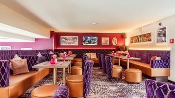 Een moderne lounge met paars en oranje zitplaatsen, tafels en kunstwerken aan de muren.