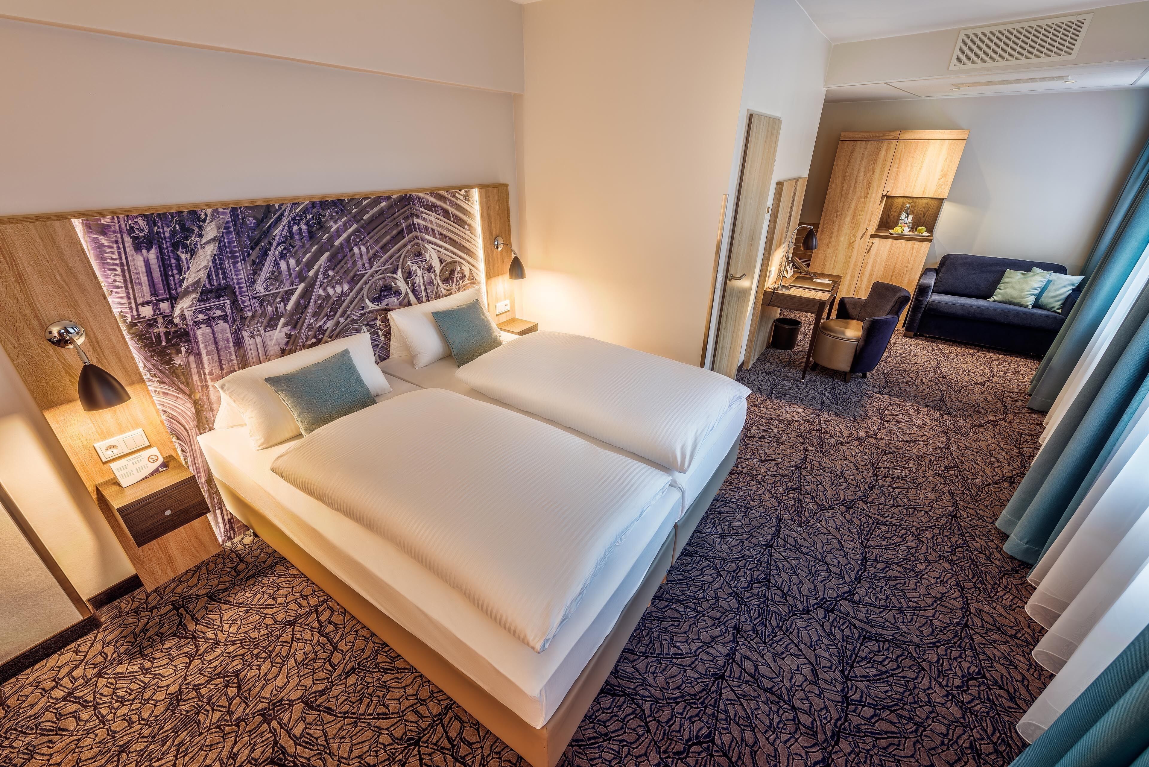 A hotel room with a large bed, a nightstand, a desk, and a sofa.