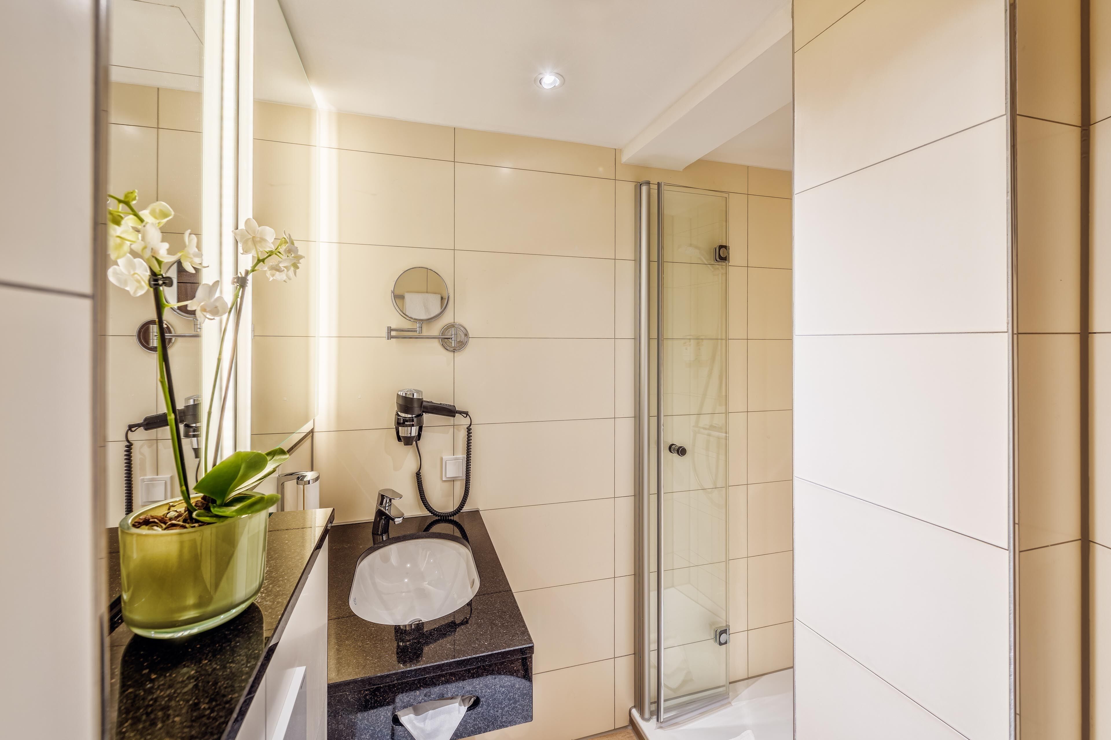A modern bathroom with a glass shower, a sink with a mirror, and a potted orchid.