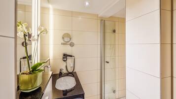 A modern bathroom with a glass shower, a sink with a mirror, and a potted orchid.