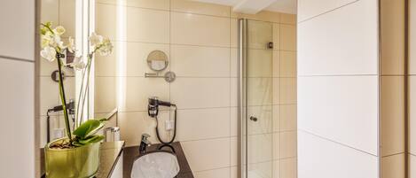 Un baño moderno con ducha de vidrio, un lavamanos con espejo y una orquídea en maceta.