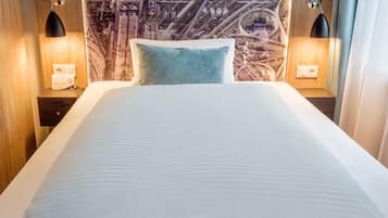 A neatly made bed with a white and blue pillow, two bedside tables with lamps, and a wall with a detailed mural.