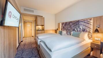 A CityClass hotel room with a large bed, a TV mounted on the wall, a wooden headboard, and a small desk with a lamp.
