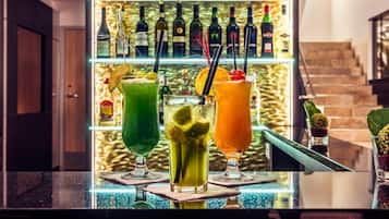 Eine Bar mit drei Cocktails, einer Wein- und Spirituosenregal sowie einer Treppe im Hintergrund.