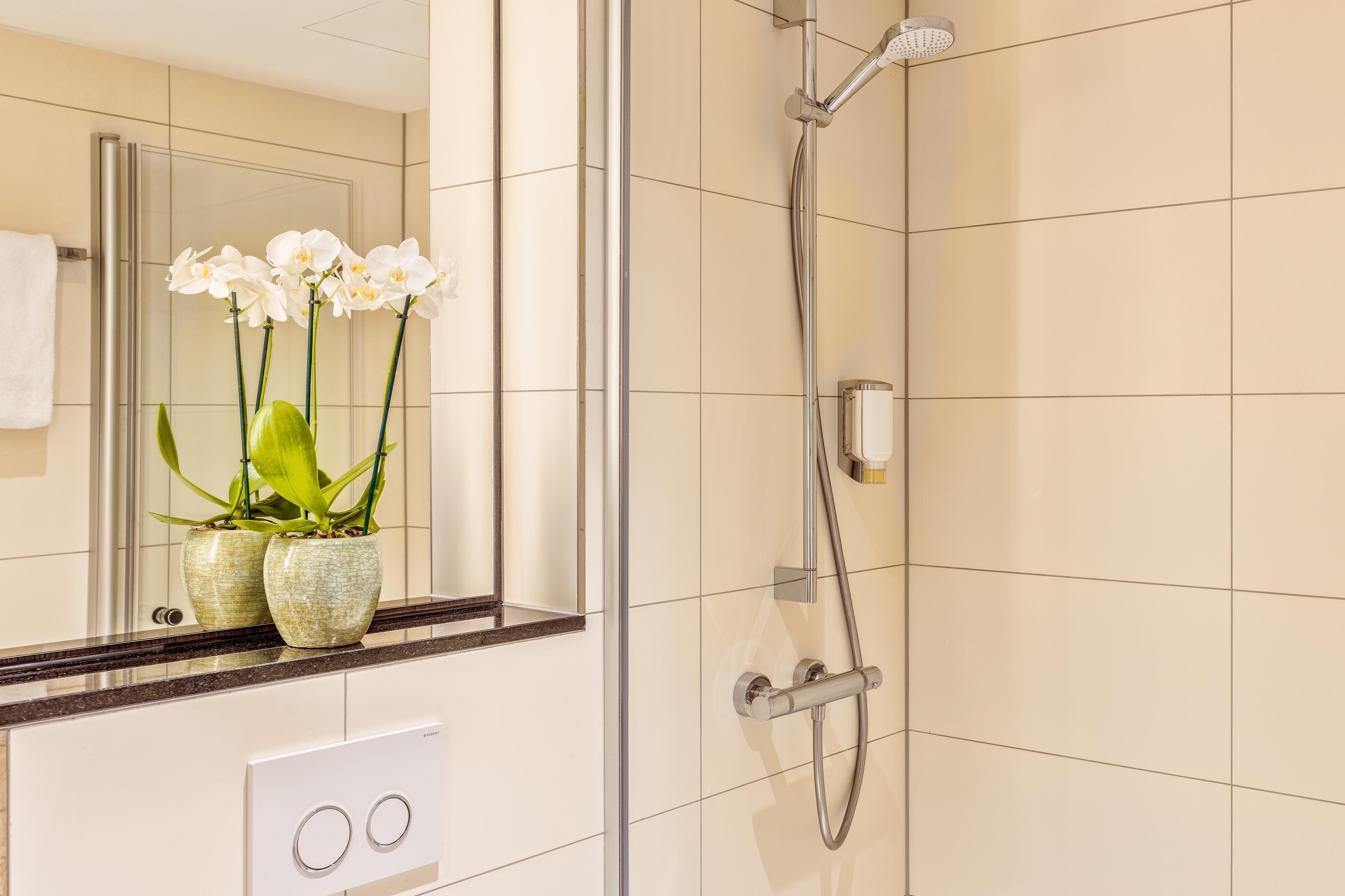 Ein Badezimmer mit Dusche, einem Spiegel und zwei Zimmerpflanzen-Orchideen.