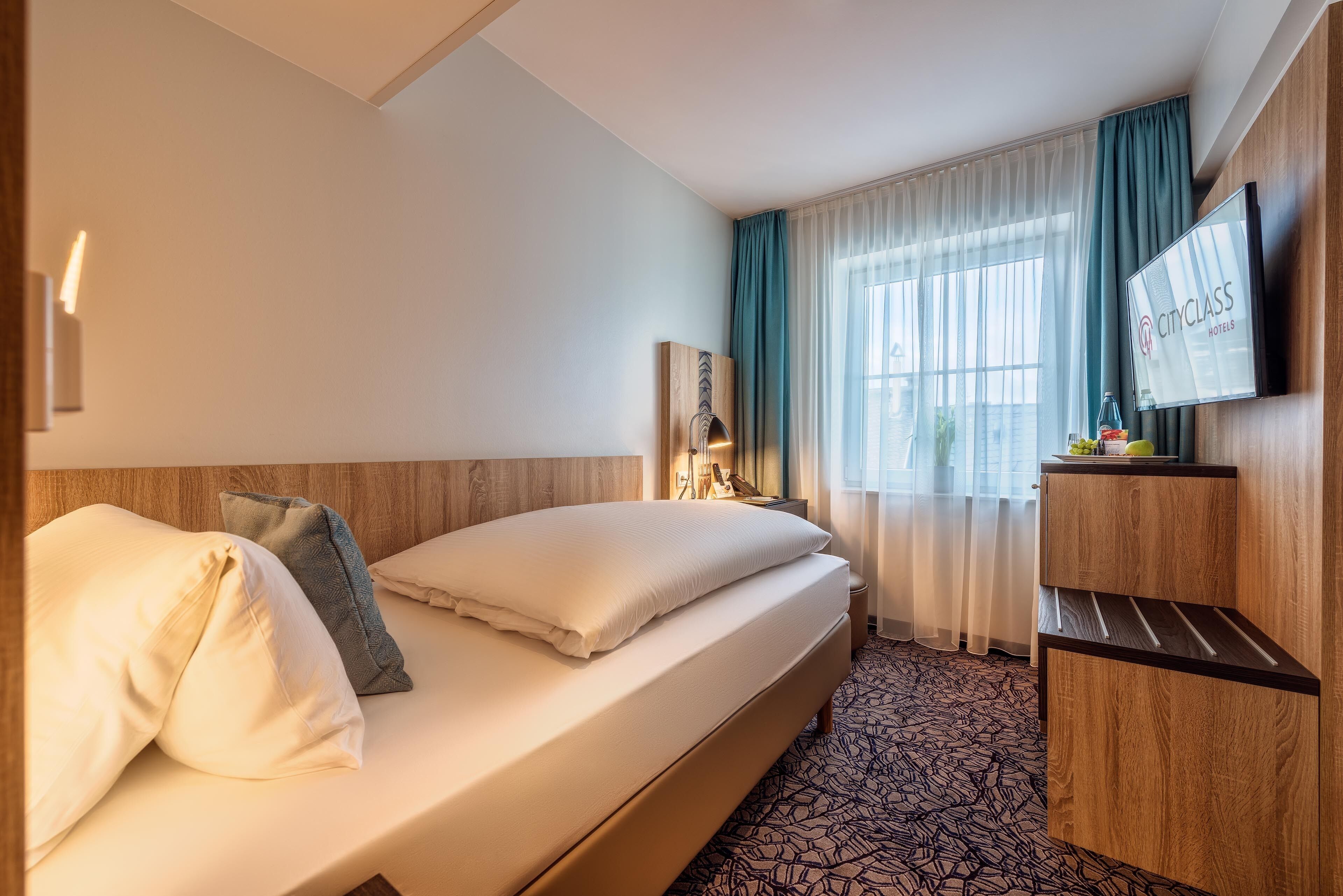 A hotel room with a bed, a TV, a nightstand, and a desk.