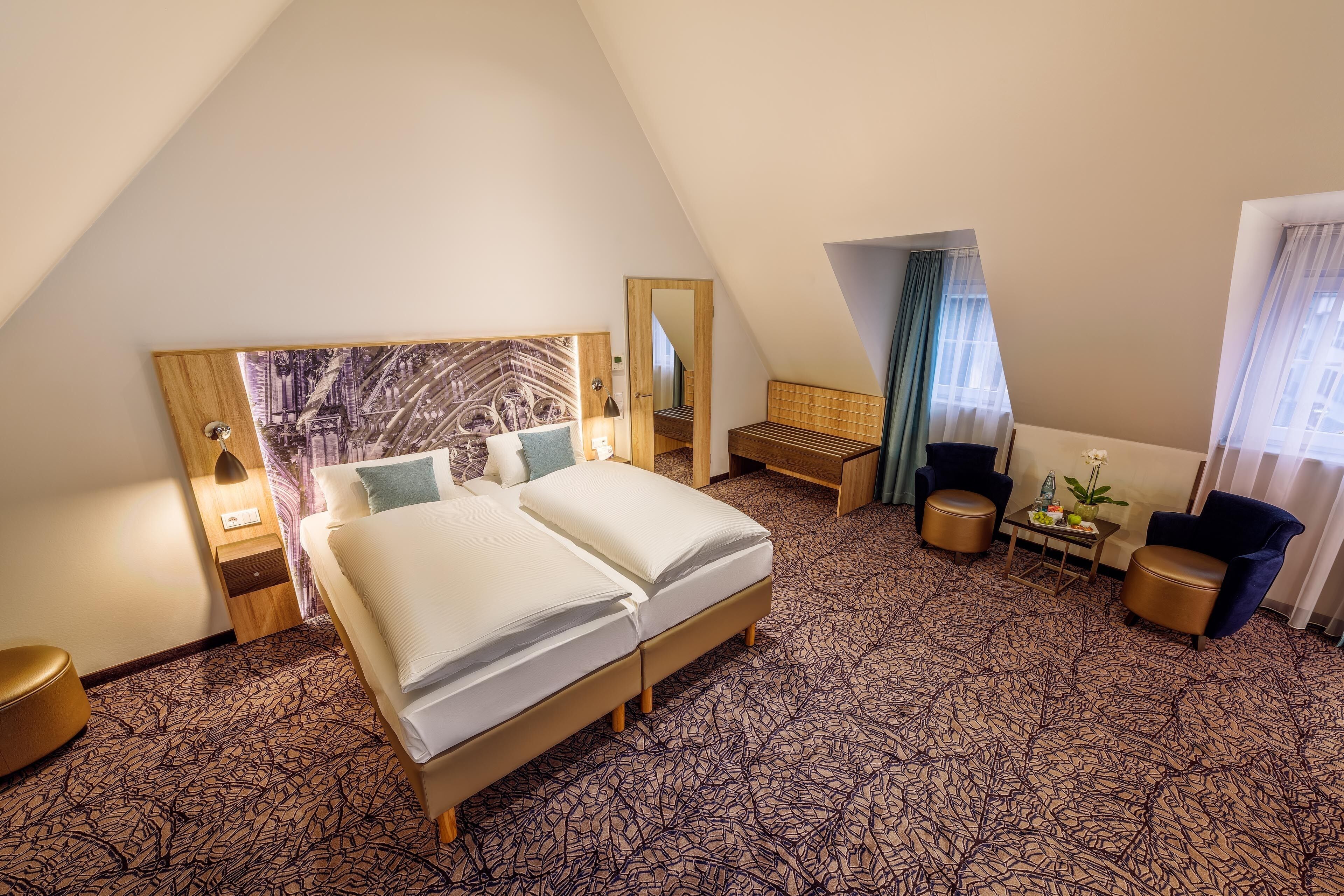 A hotel room with a bed, a desk, a chair, and a small table with a vase of flowers.