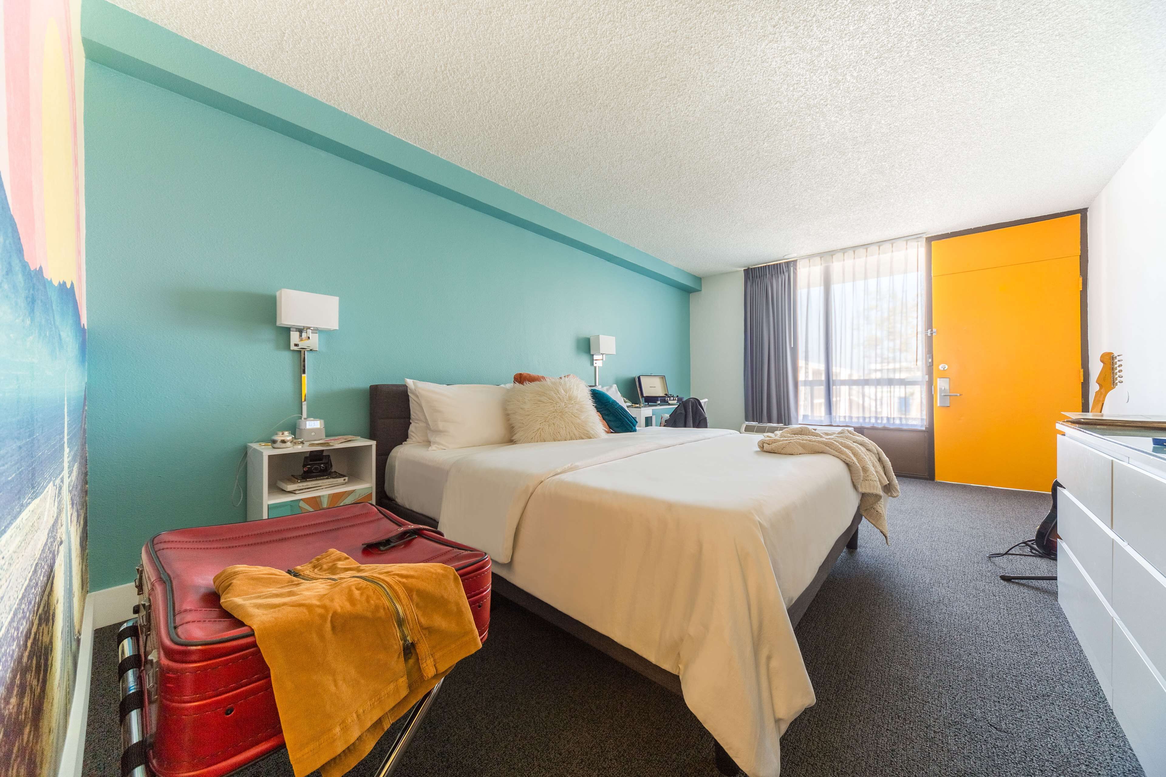 A hotel room with two beds, a desk, a chair, a wardrobe, a nightstand, a lamp, and a suitcase.