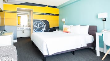 A hotel room with a bed, a desk, a chair, a mirror, and a wall with a car decal.