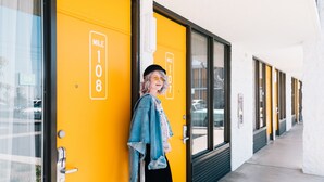A person leaning against a yellow door with "MILE 108" signage, indicating a location or landmark.