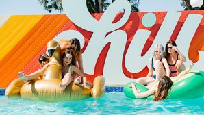 A group of people on inflatable floats in a pool with a colorful backdrop.