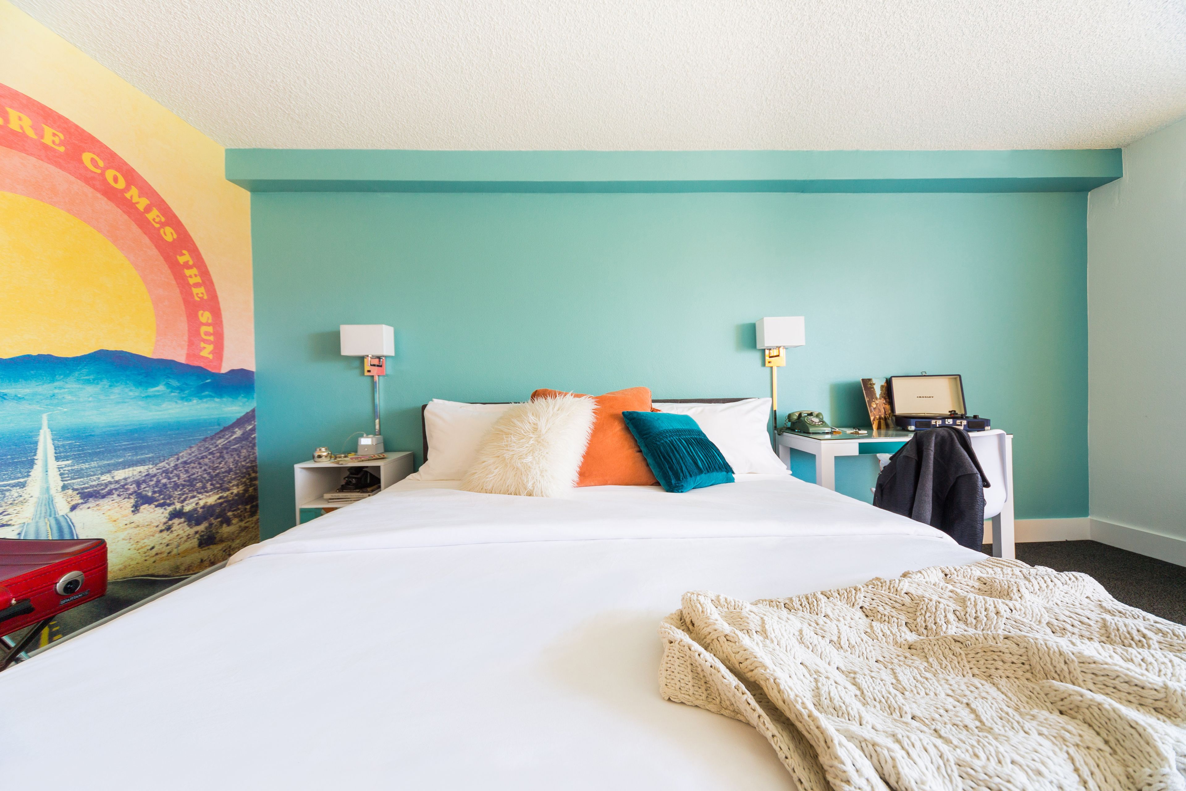 A hotel room with a large bed, two bedside tables, a desk, and a mural on the wall.