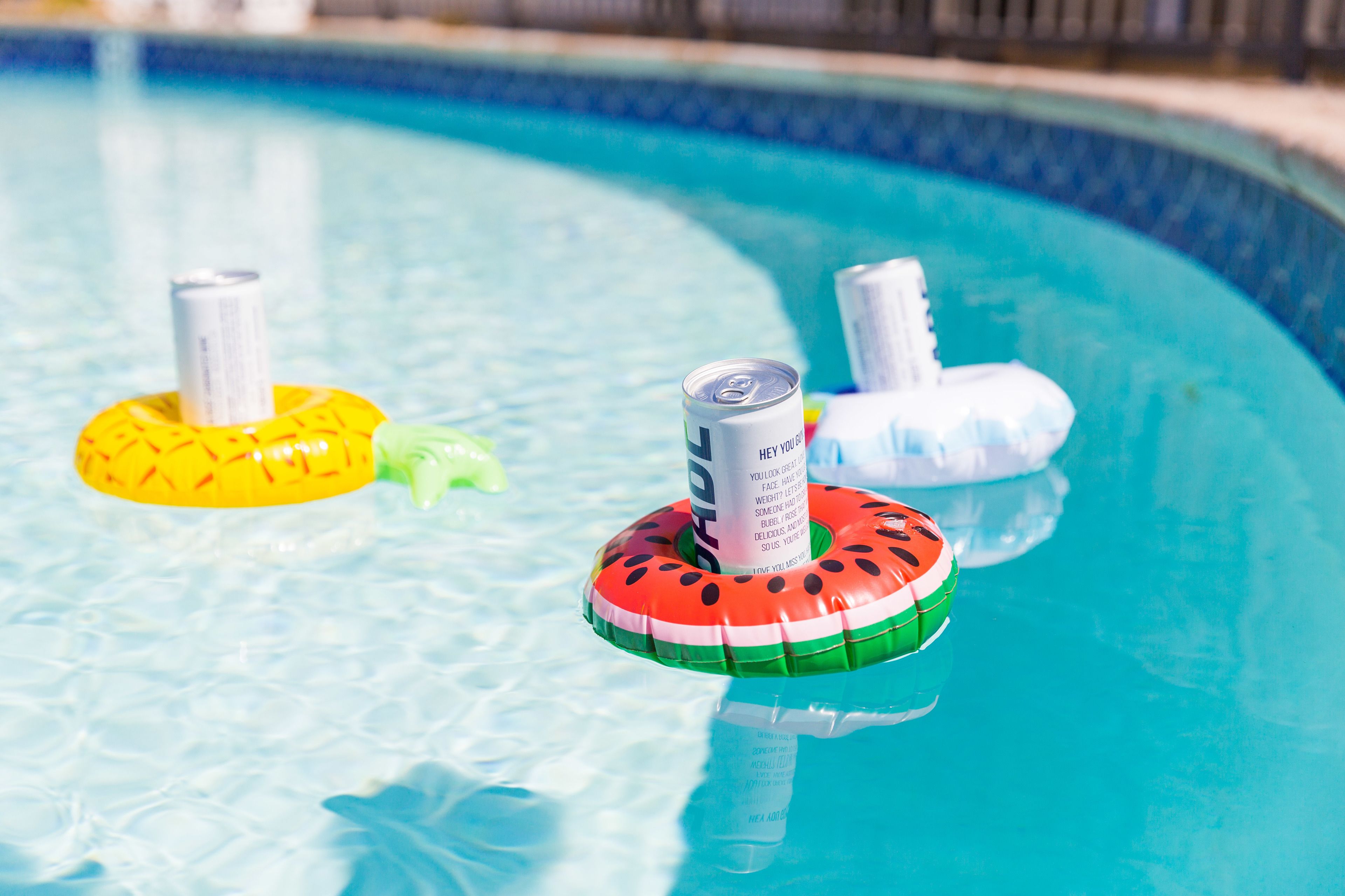 A swimming pool with three inflatable rings, one yellow, one green, and one watermelon-patterned.