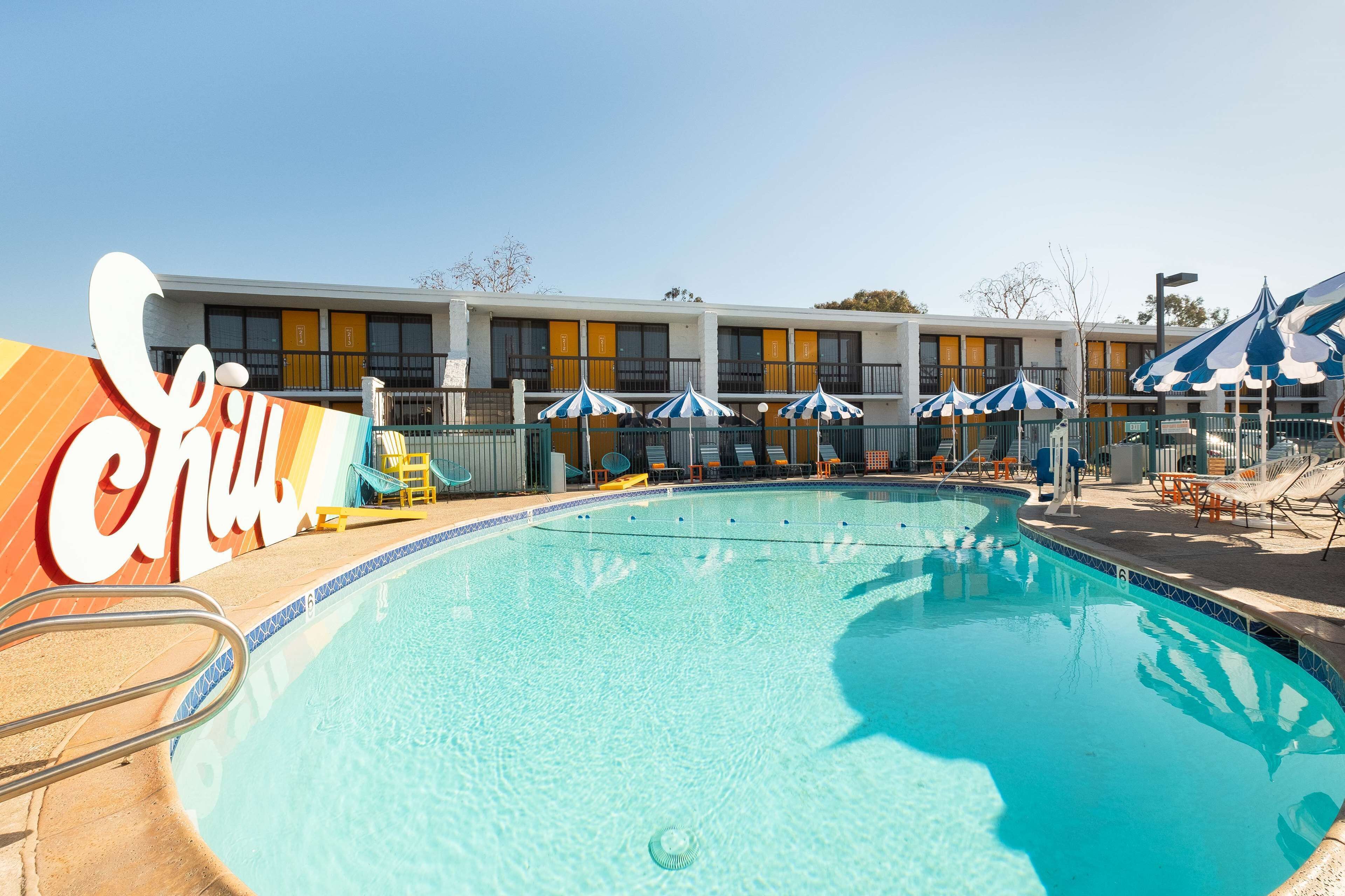 A swimming pool with lounge chairs and umbrellas, a building with yellow windows, and a large 'Club' sign.
