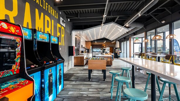 A retro-themed arcade with classic games, a foosball table, and a long communal table with stools.