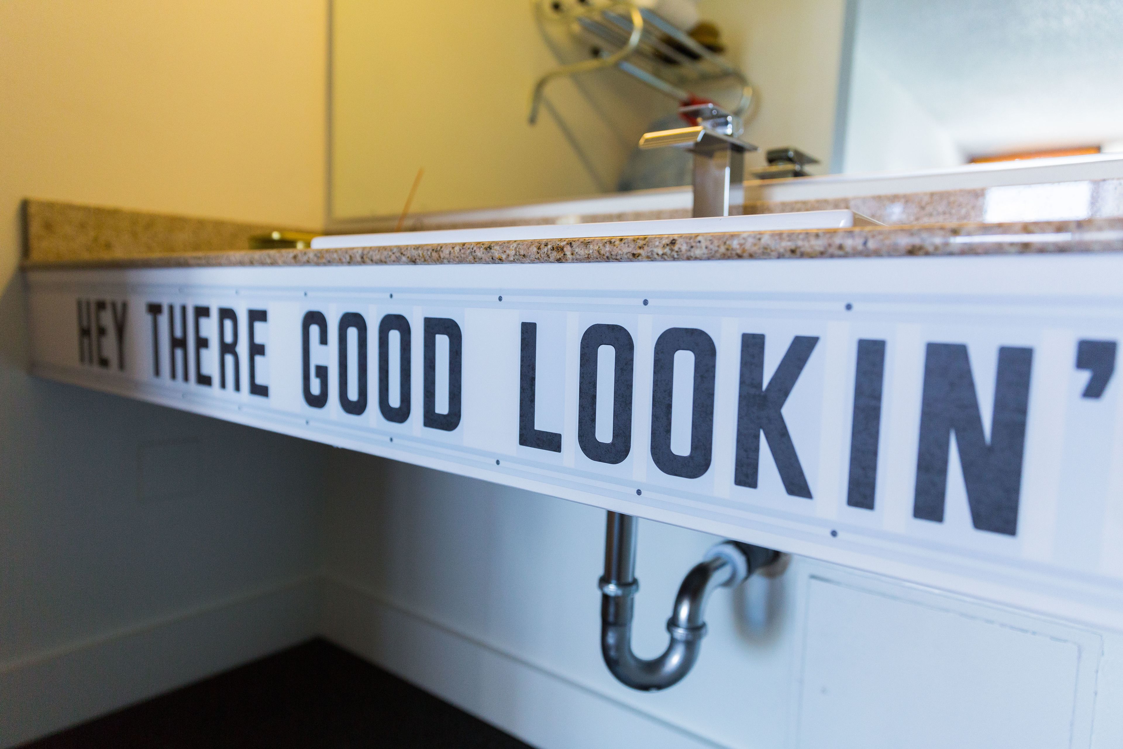 A bathroom with a sink and a sign above it that reads "HEY THERE GOOD LOOKIN'".