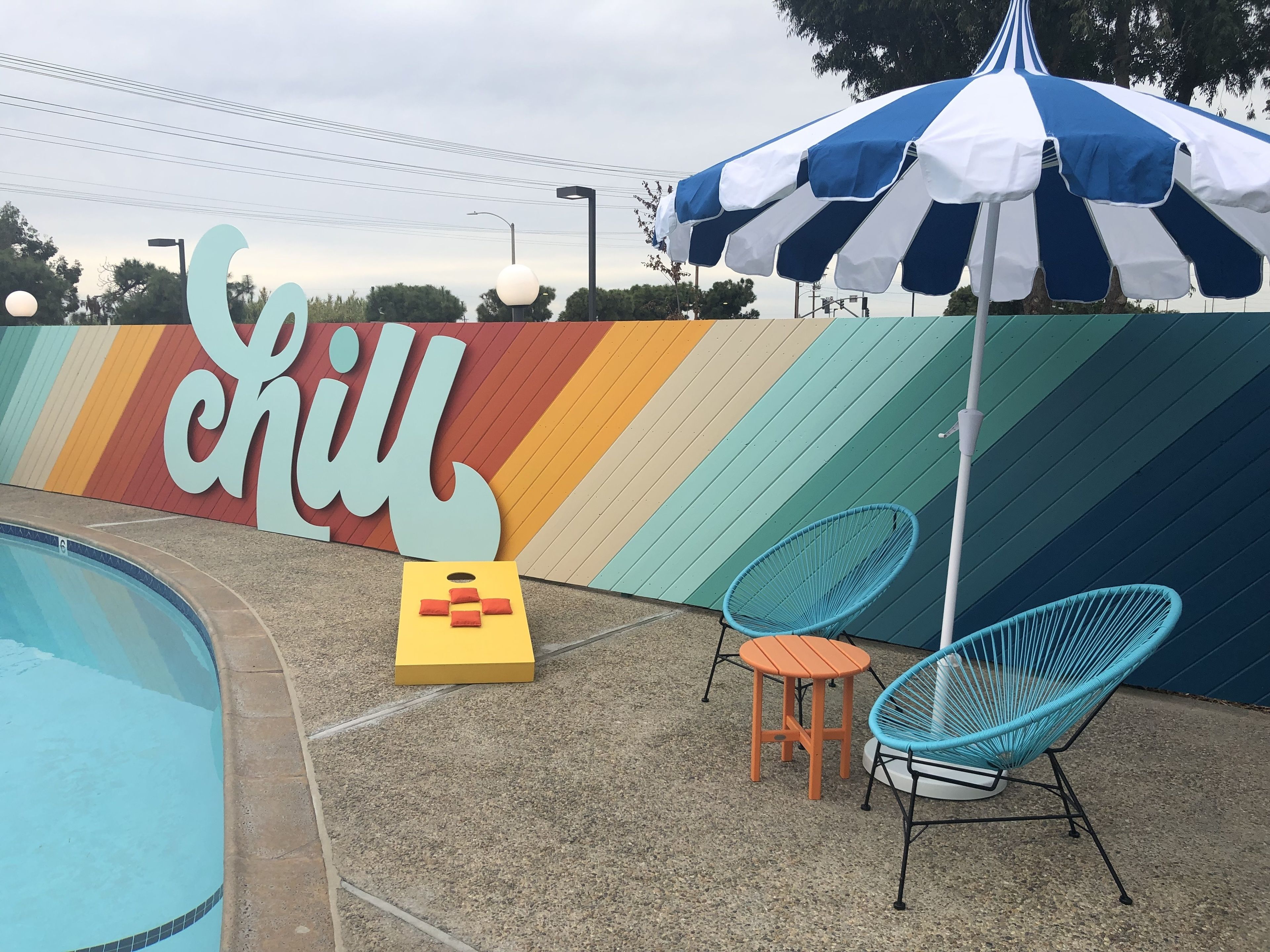 A pool area with a colorful wall, a striped umbrella, and two chairs.