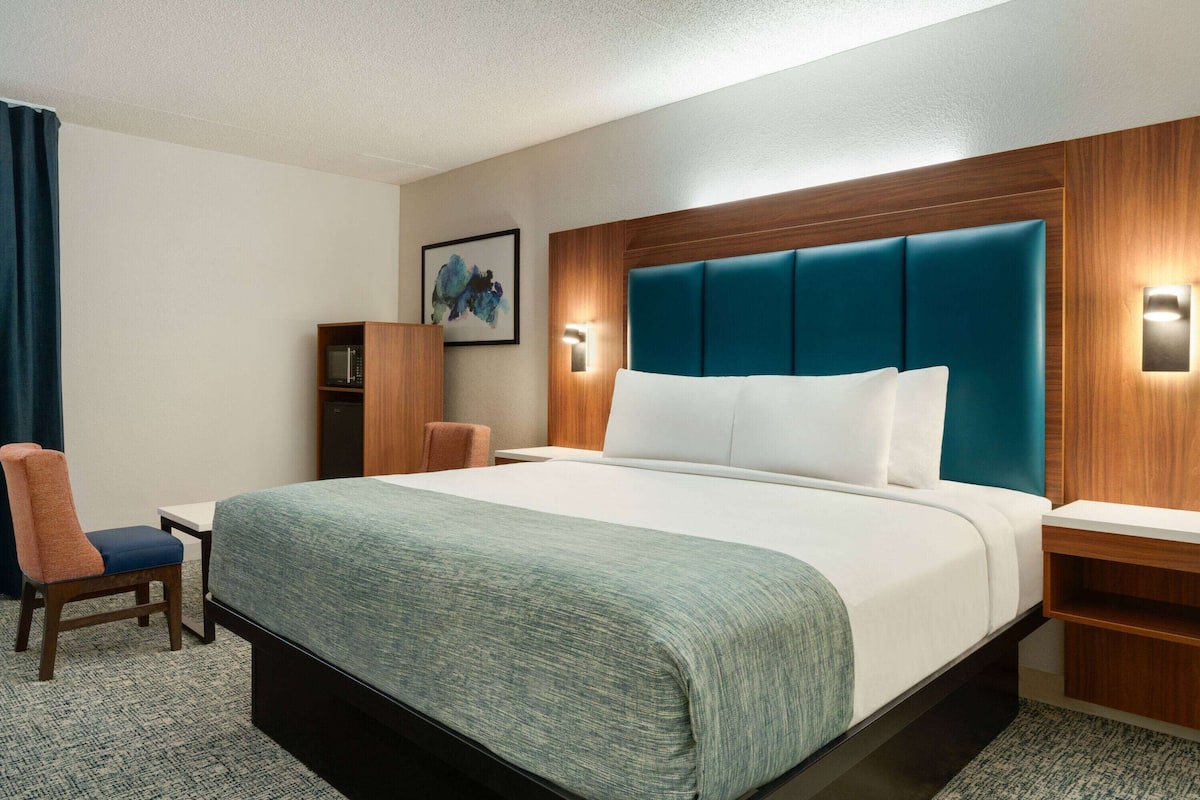 Een hotelkamer met een groot bed, een houten hoofdbord, een nachtkastje, een stoel, een kleine tafel en een wandplank.