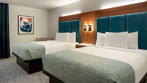 Une chambre d’hôtel avec deux lits, une tête de lit en bois, une table de chevet, un tableau encadré et une fenêtre avec des rideaux.