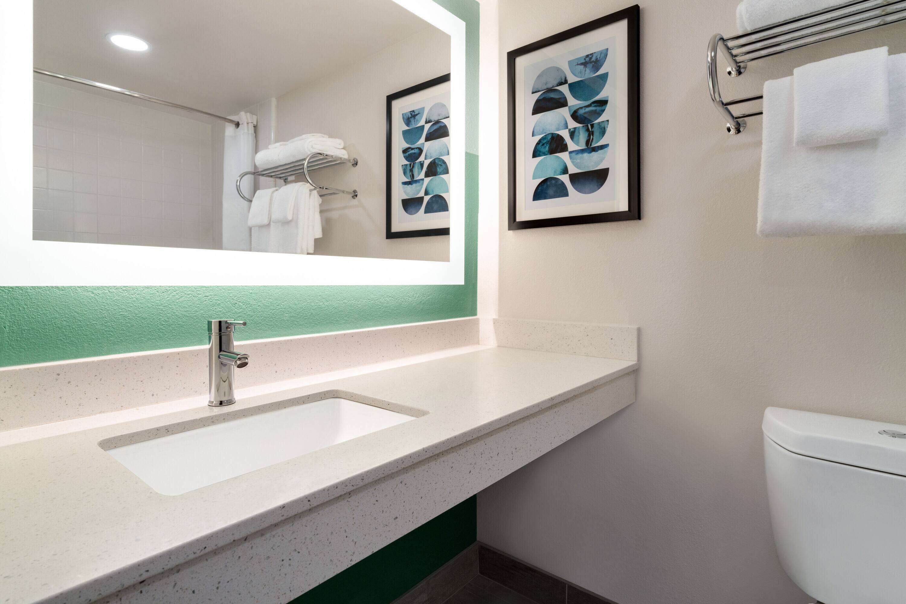 A bathroom with a white sink, a mirror, and a toilet. There are framed pictures on the wall and a towel rack with towels.