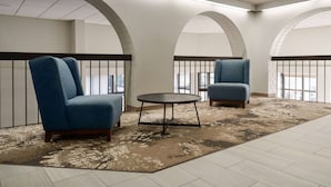 Un salon moderne avec deux fauteuils bleus et une petite table ronde, agrémenté d’un tapis à motifs et offrant une vue à travers la balustrade d’un balcon.
