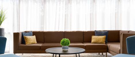 A modern living room with a brown sectional sofa, a round coffee table, and blue armchairs.