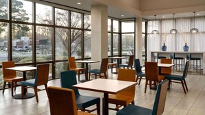 Un espace repas moderne doté de grandes fenêtres, de plusieurs tables et chaises, et offrant une vue sur l’extérieur.