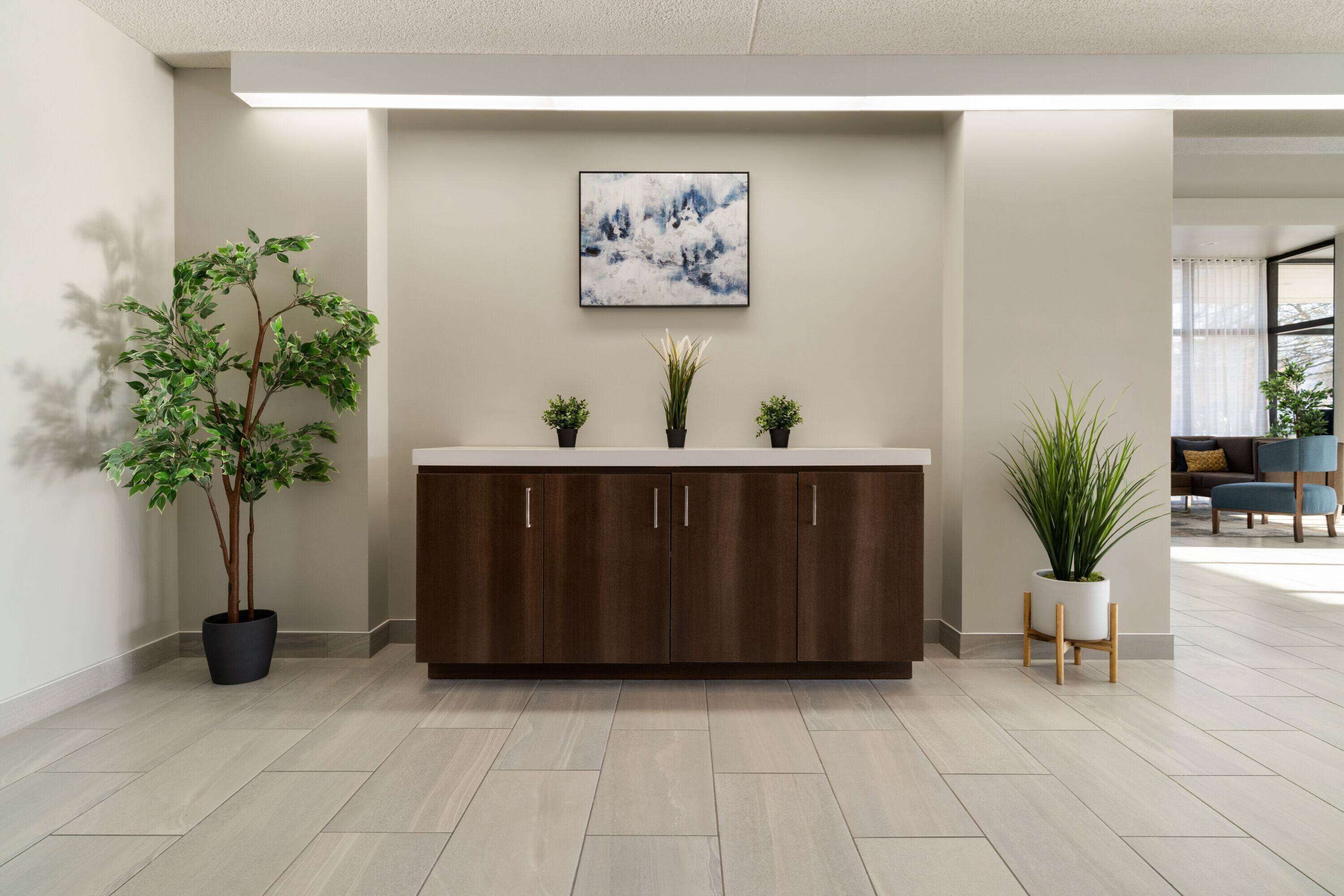 A reception area with a wooden cabinet, a large abstract painting, and potted plants.