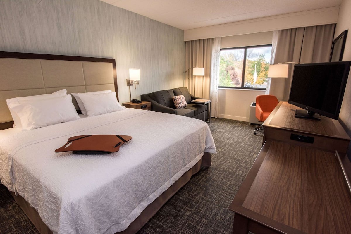 A hotel room with a large bed, a desk with a TV, a chair, and a window with curtains.