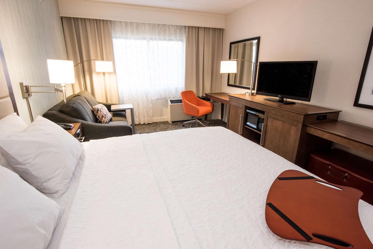 A hotel room with a large bed, a desk with a television, a chair, and a desk lamp.