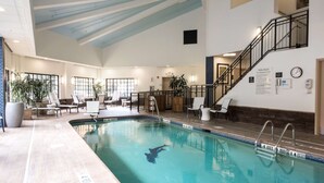Ein Hallenbad mit Rettungsschwimmerstuhl, Liegestühlen und einer Treppe.