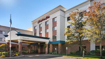 Um hotel Hampton Inn com entrada acessível, área de espera coberta e fachada de tijolos.