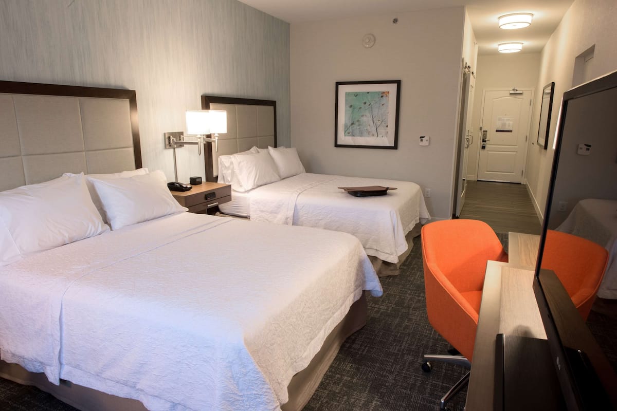A hotel room with two beds, a desk, a chair, and a television.