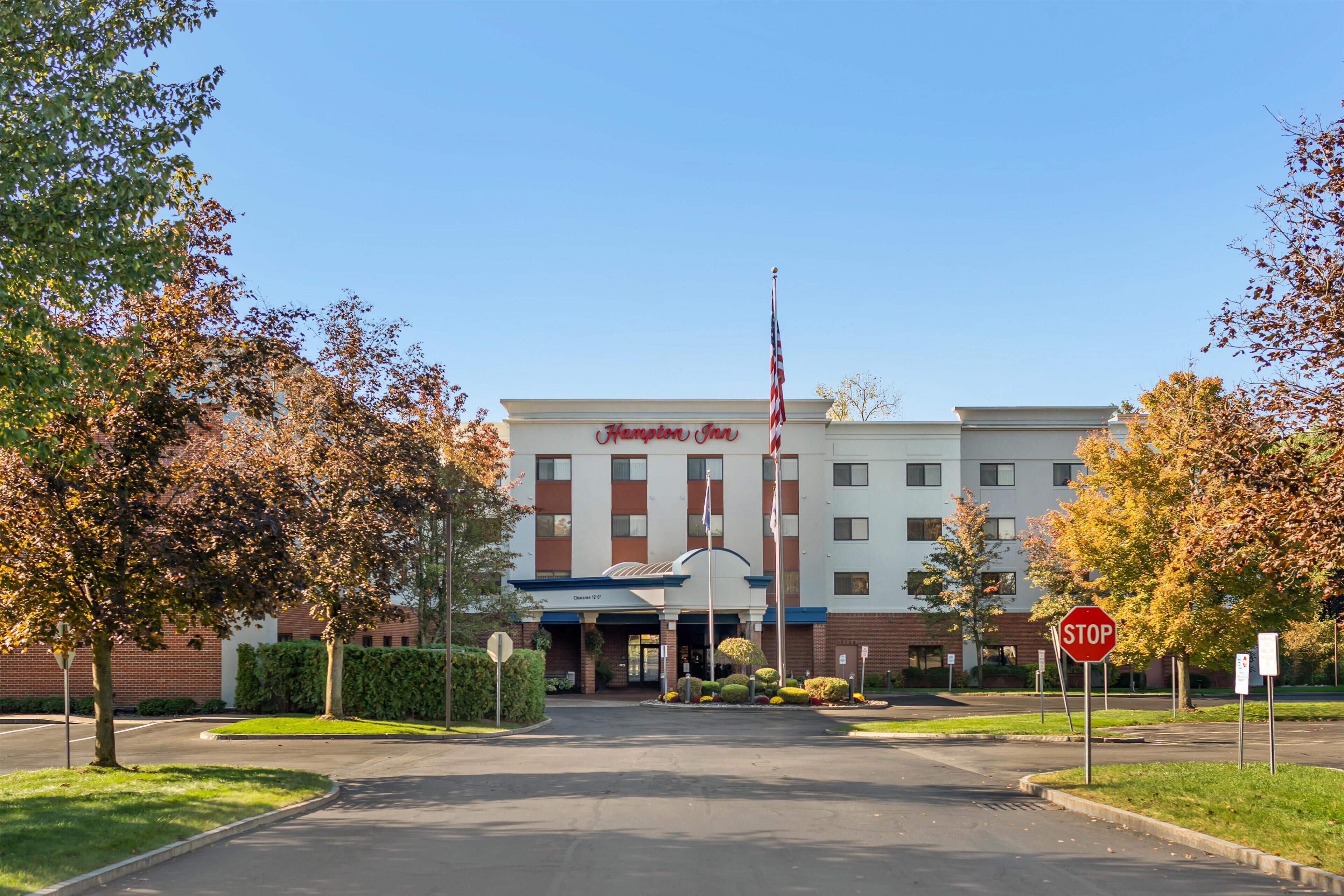A Hampton Inn hotel entrance with a clear sky, autumn foliage, and a stop sign.