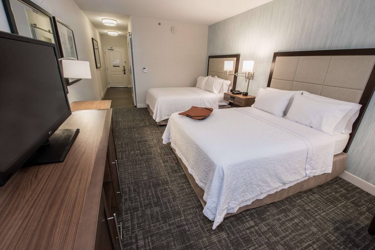 A hotel room with two beds, a flat-screen TV, a desk, and a mirror.