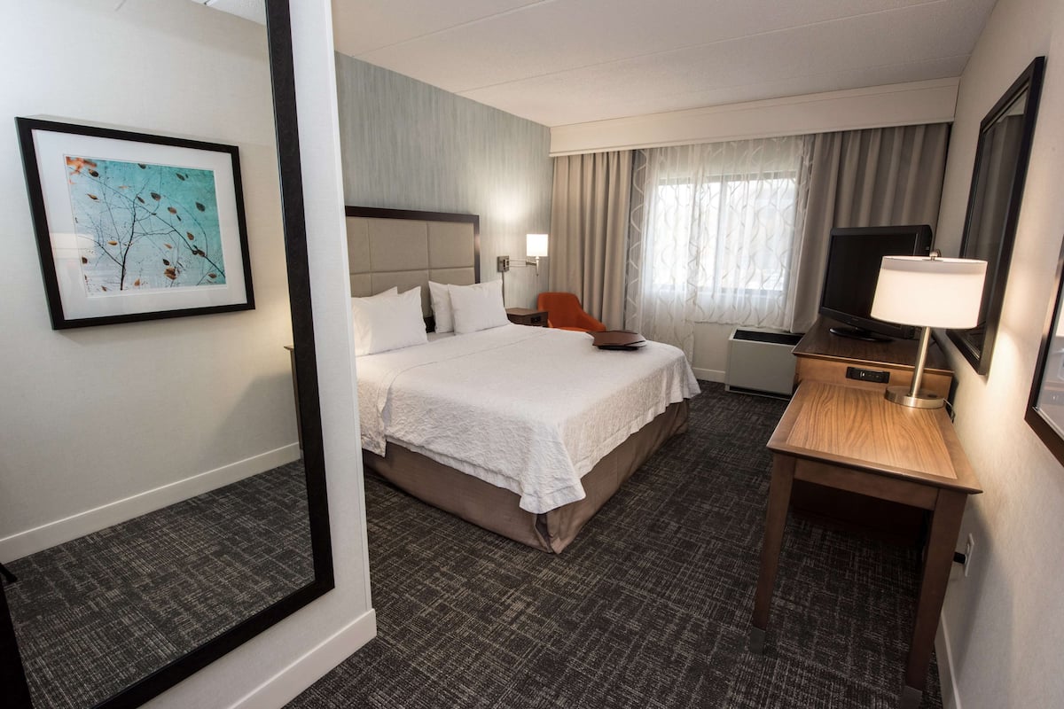 A hotel room with a large bed, a desk with a TV, a chair, and a framed picture on the wall.
