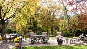 Ein Patio im Freien mit Tischen und Stühlen, umgeben von Bäumen mit Herbstlaub.