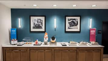 A buffet setup with various food items and appliances, framed pictures on the wall, and a blue sign with text.