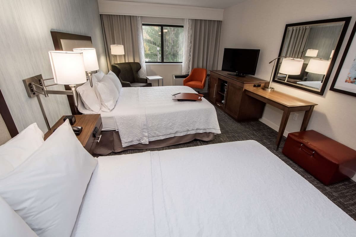 A hotel room with two beds, a desk, a chair, a TV, and a mirror.
