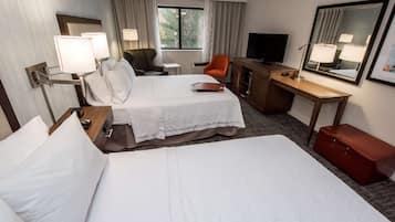 A hotel room with two beds, a desk, a chair, a television, and a mirror.
