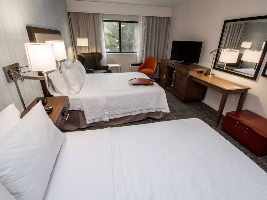 A hotel room with two beds, a desk, a chair, a television, and a mirror.